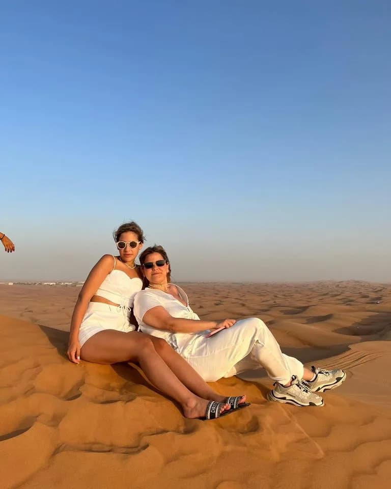 Two guests relaxing on a sand dune under a clear blue sky