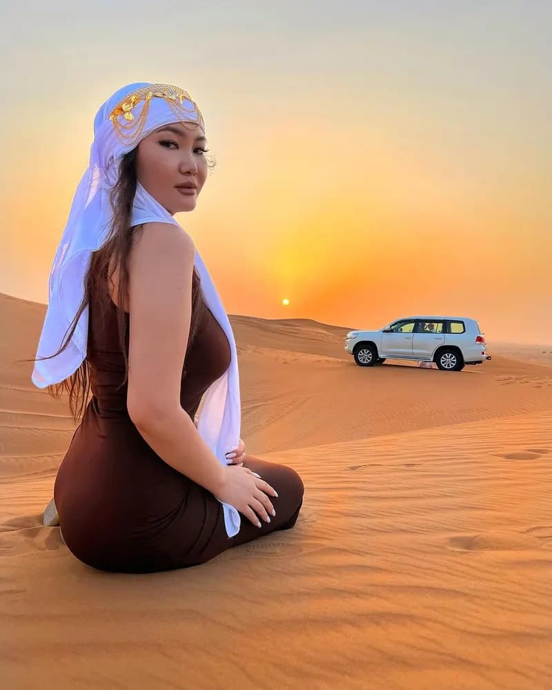 Guest in a headscarf sitting on the dunes at sunset