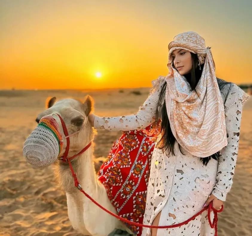 Guest walking a camel across the desert at sunset