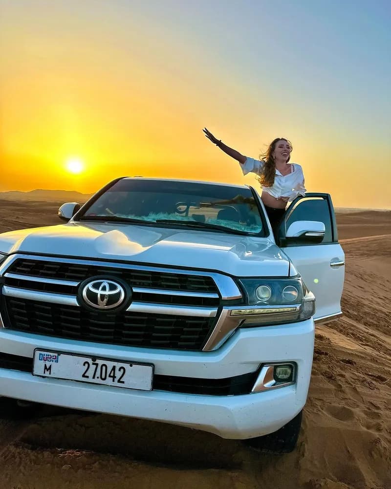 Guest waving from a safari 4x4 on the dunes at sunset