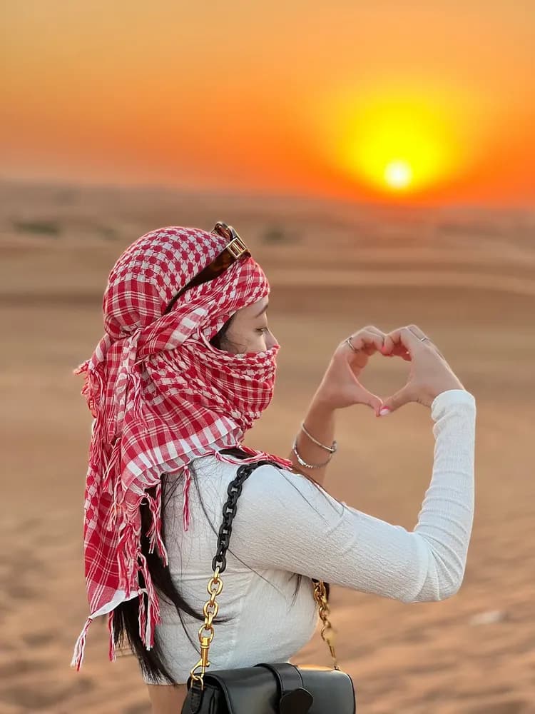 Guest in a keffiyeh making a heart towards the desert sunset