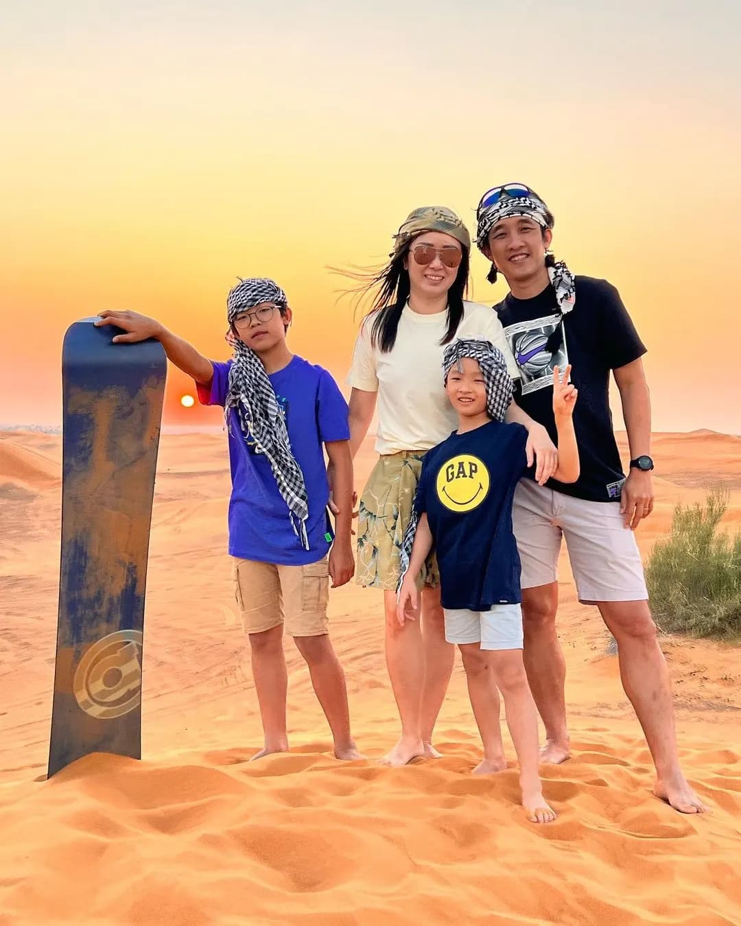 Family with sandboards on the dunes at sunset