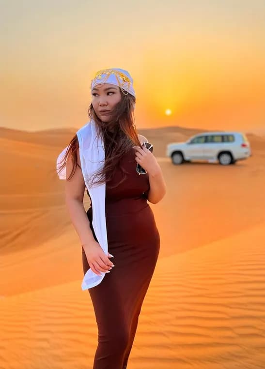 Woman posing on red desert dunes at sunset with a safari 4x4 behind her in Dubai